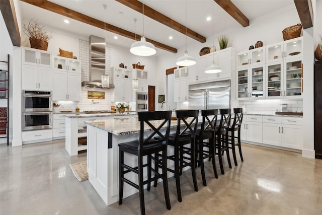 kitchen featuring built in appliances, a large island with sink, concrete floors, and wall chimney range hood