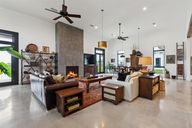 living area with a ceiling fan, a high ceiling, concrete flooring, and a fireplace