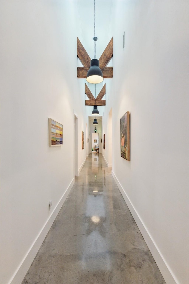 hallway featuring a high ceiling, baseboards, visible vents, and finished concrete flooring