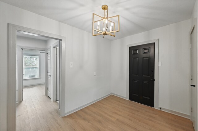 entryway with baseboards, an inviting chandelier, and light wood finished floors