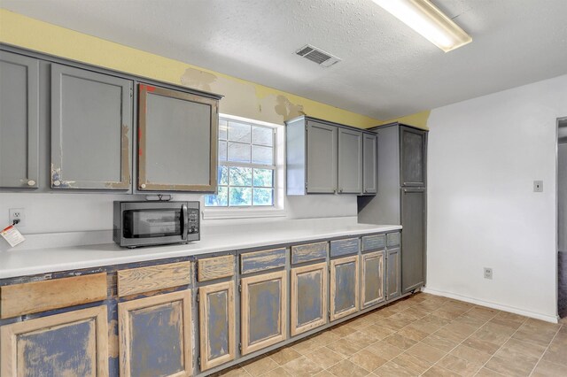 kitchen with stainless steel microwave, visible vents, baseboards, and light countertops