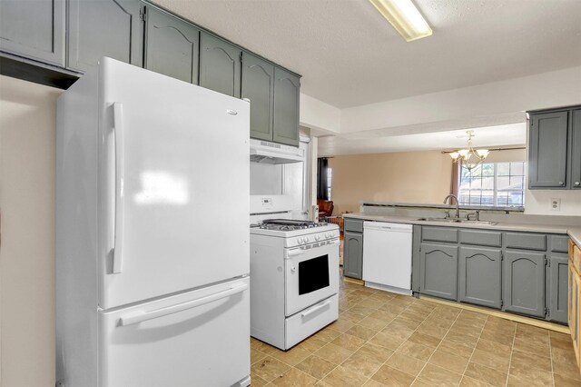 kitchen featuring a sink, a chandelier, under cabinet range hood, a peninsula, and white appliances