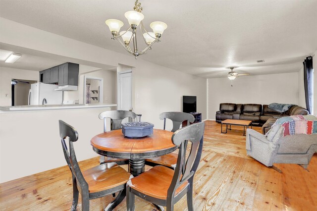 dining area featuring ceiling fan with notable chandelier and light wood-style floors
