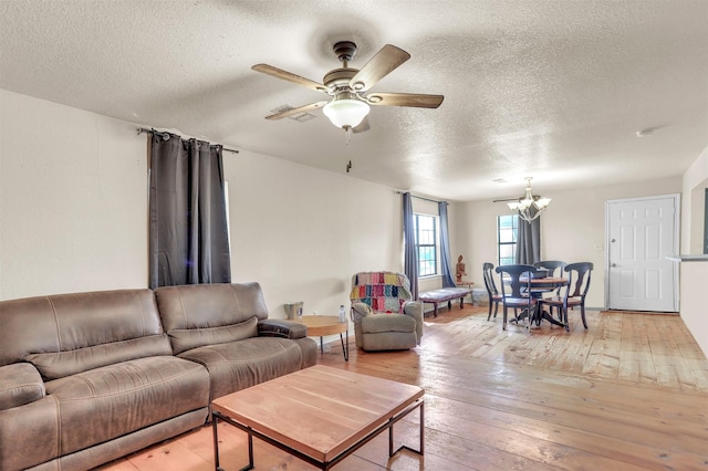 living area featuring ceiling fan with notable chandelier, a textured ceiling, and light wood finished floors