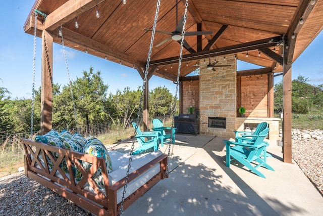 view of patio / terrace featuring fence, ceiling fan, a gazebo, a grill, and an outdoor stone fireplace