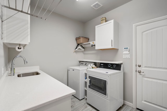 laundry room featuring a sink, cabinet space, washer and clothes dryer, visible vents, and light wood-style flooring