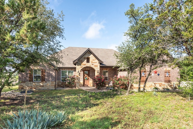 tudor-style house with roof with shingles, a front lawn, and stone siding