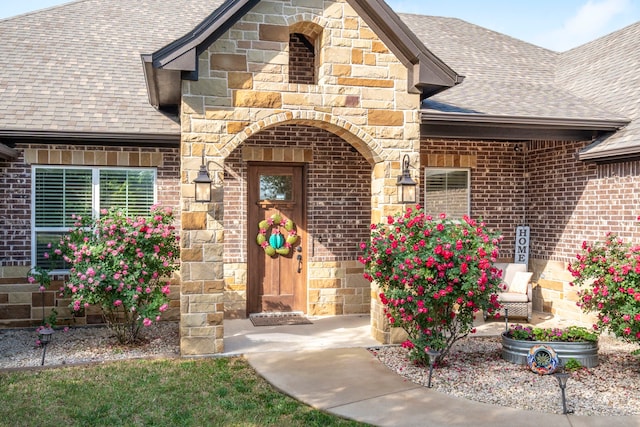 doorway to property featuring brick siding, a shingled roof, and stone siding