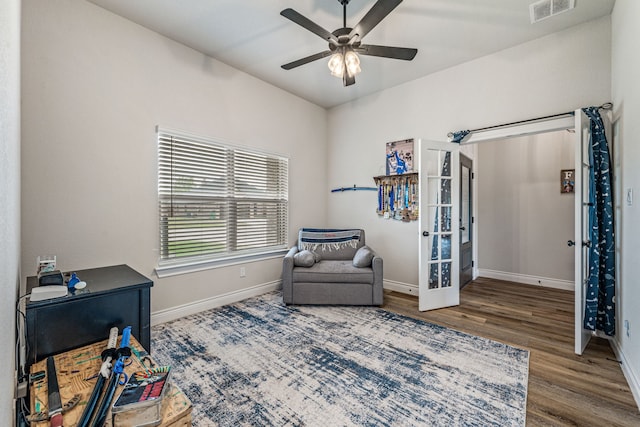 living area featuring baseboards, visible vents, wood finished floors, and ceiling fan