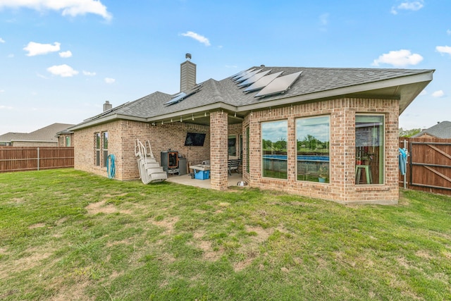 back of house featuring a patio, a fenced backyard, a lawn, brick siding, and solar panels