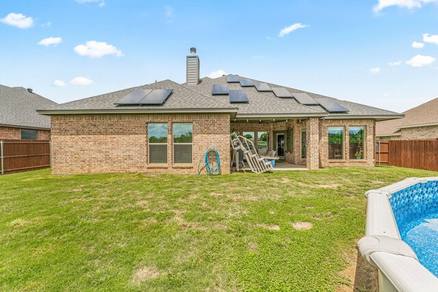 rear view of property featuring roof with shingles, brick siding, solar panels, and a fenced backyard