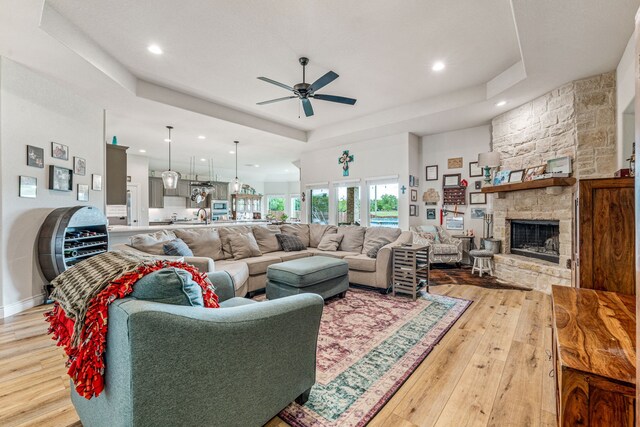 living area featuring a fireplace, a raised ceiling, a ceiling fan, and light wood-style flooring