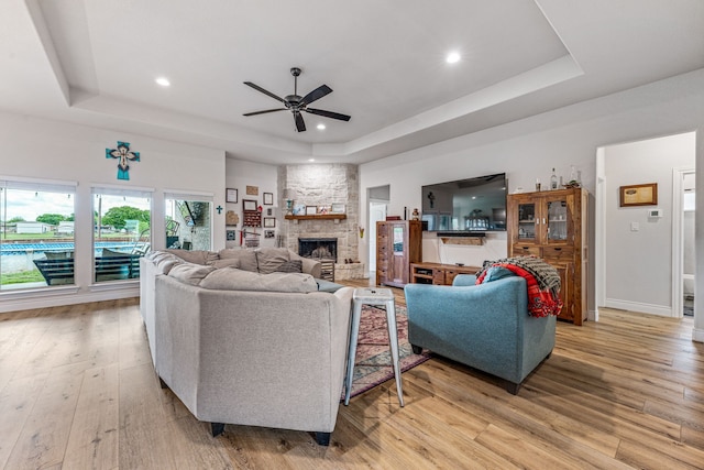 living area with recessed lighting, ceiling fan, light wood finished floors, a fireplace, and a tray ceiling