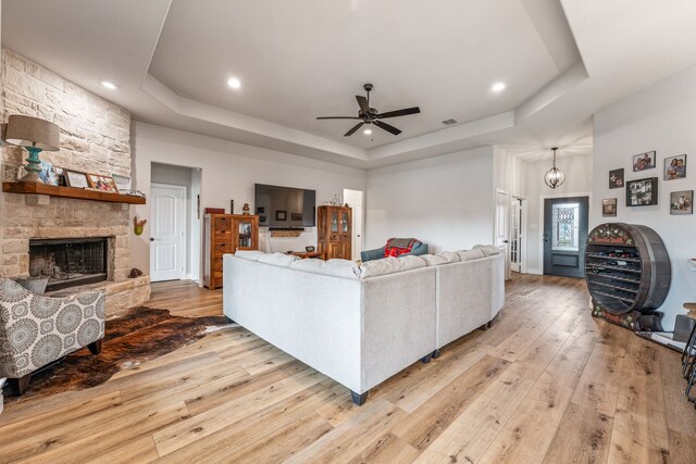 living area featuring a raised ceiling, light wood-type flooring, recessed lighting, a fireplace, and a ceiling fan