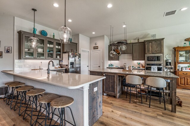 kitchen featuring a breakfast bar area, light wood-style flooring, a sink, appliances with stainless steel finishes, and backsplash