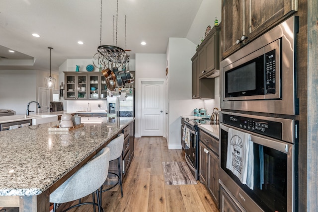 kitchen featuring glass insert cabinets, light wood-type flooring, a breakfast bar, light stone counters, and appliances with stainless steel finishes