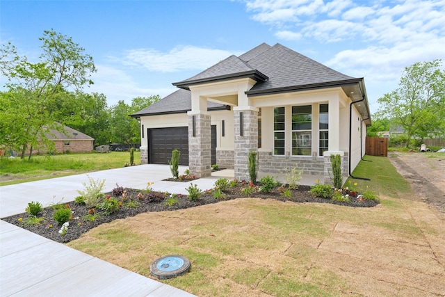 prairie-style house with fence, a front yard, stone siding, an attached garage, and driveway
