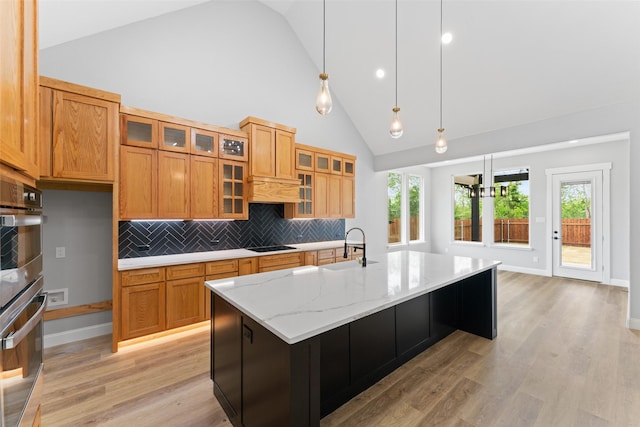 kitchen with a sink, high vaulted ceiling, light wood-type flooring, backsplash, and pendant lighting