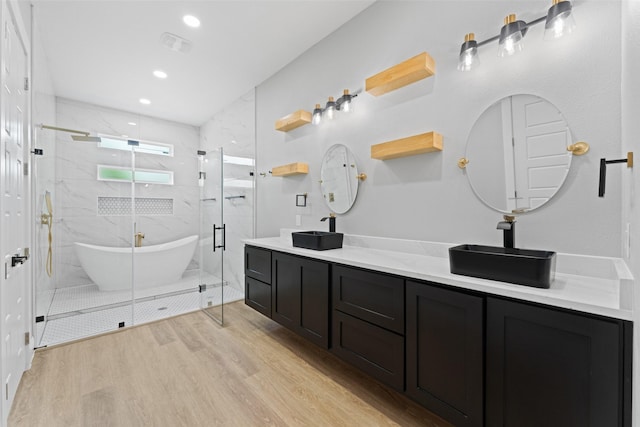 full bath with double vanity, a marble finish shower, wood finished floors, and a soaking tub