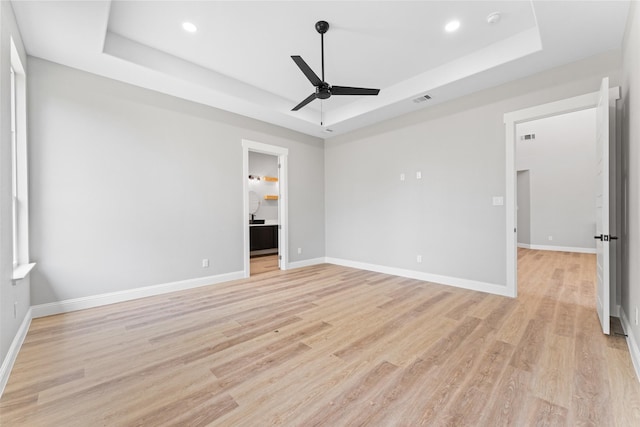unfurnished bedroom with recessed lighting, a tray ceiling, baseboards, and light wood-style floors