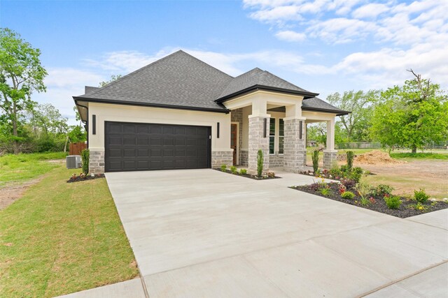 prairie-style home with a shingled roof, central AC, stone siding, a garage, and driveway