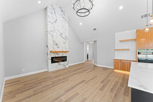 unfurnished living room with high vaulted ceiling, visible vents, a premium fireplace, and a chandelier