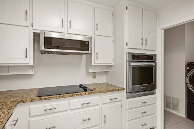 kitchen featuring appliances with stainless steel finishes, white cabinetry, washer / clothes dryer, light tile patterned flooring, and stone countertops