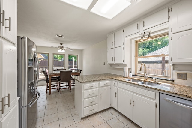 kitchen featuring stainless steel appliances, a sink, light tile patterned flooring, white cabinets, and plenty of natural light