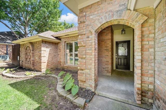 doorway to property featuring brick siding and roof with shingles