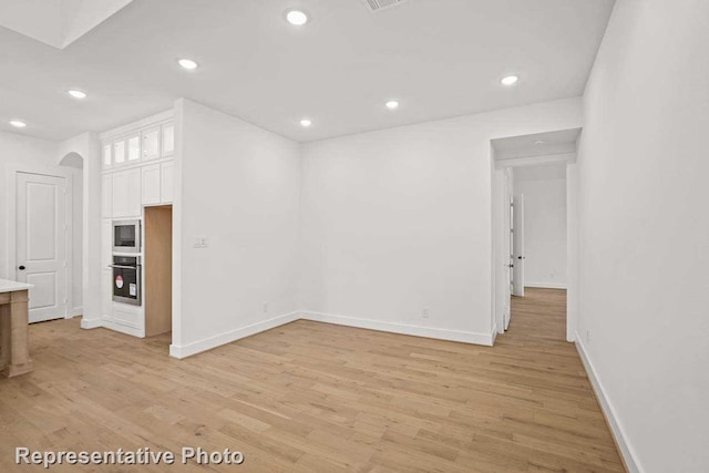 interior space featuring light wood-type flooring, recessed lighting, arched walkways, and baseboards