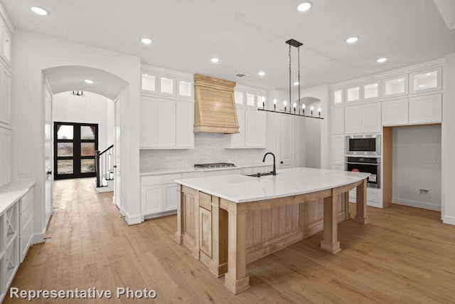 kitchen with arched walkways, appliances with stainless steel finishes, light wood-style flooring, and premium range hood