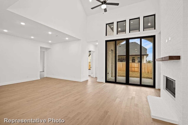 unfurnished living room featuring baseboards, a fireplace, a towering ceiling, wood finished floors, and a ceiling fan