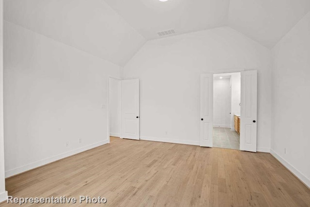 unfurnished bedroom featuring vaulted ceiling, visible vents, light wood-style flooring, and baseboards