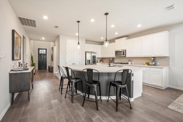 kitchen with appliances with stainless steel finishes, a sink, backsplash, wood finished floors, and light countertops