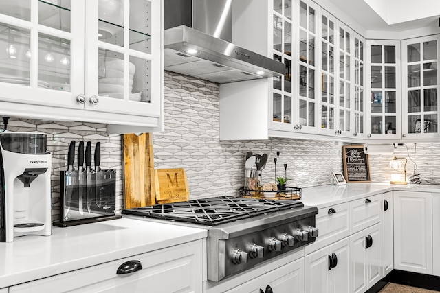 kitchen with stainless steel gas cooktop, glass insert cabinets, wall chimney range hood, backsplash, and white cabinetry