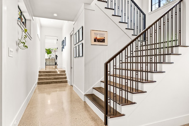 staircase featuring baseboards, ornamental molding, a wealth of natural light, and speckled floor