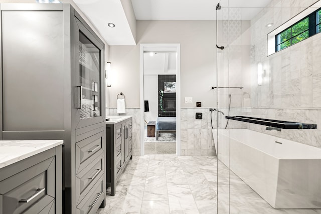full bath featuring connected bathroom, tile walls, vanity, a freestanding bath, and marble finish floor