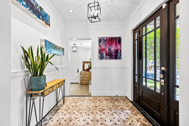 entrance foyer featuring ornamental molding, a wainscoted wall, an inviting chandelier, and a decorative wall