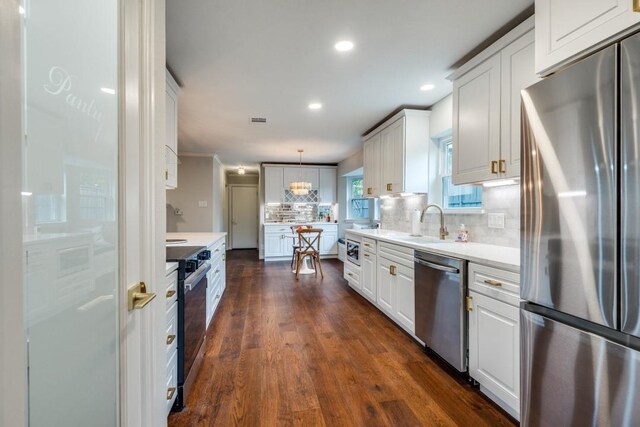 kitchen featuring a sink, dark wood-type flooring, tasteful backsplash, white cabinetry, and appliances with stainless steel finishes
