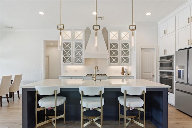 kitchen featuring stainless steel fridge, light countertops, backsplash, visible vents, and a center island with sink