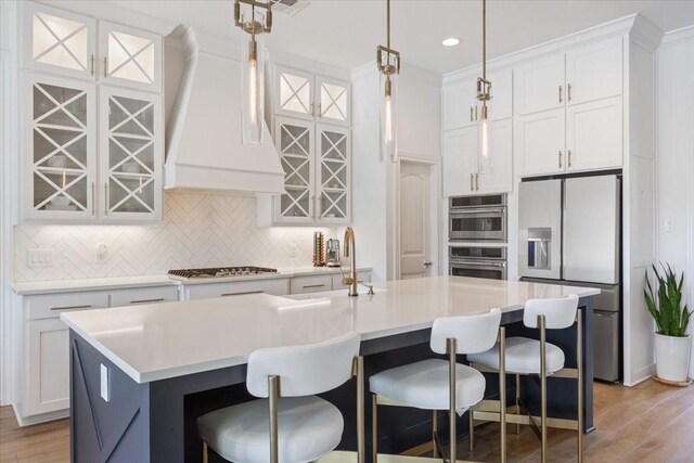 kitchen with stainless steel appliances, tasteful backsplash, white cabinetry, light countertops, and an island with sink