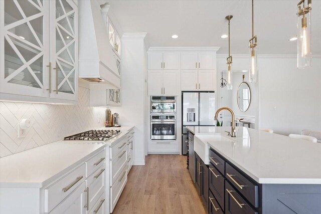 kitchen featuring white cabinetry, glass insert cabinets, a sink, appliances with stainless steel finishes, and light countertops