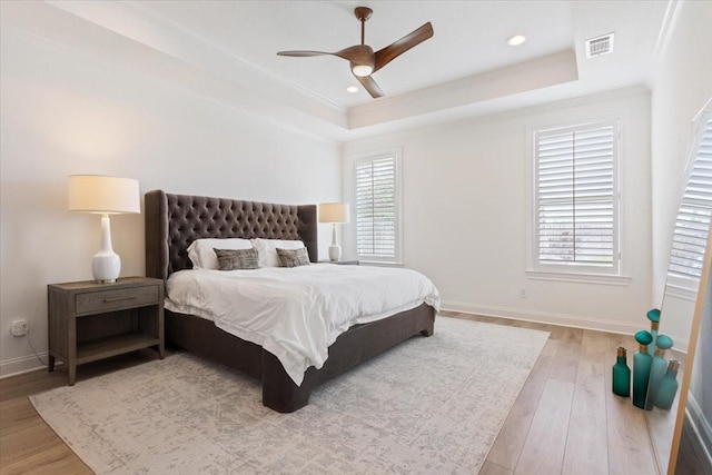 bedroom featuring a raised ceiling, a ceiling fan, visible vents, baseboards, and wood finished floors