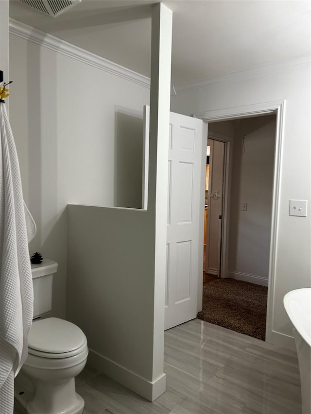 bathroom featuring baseboards, ornamental molding, visible vents, and toilet