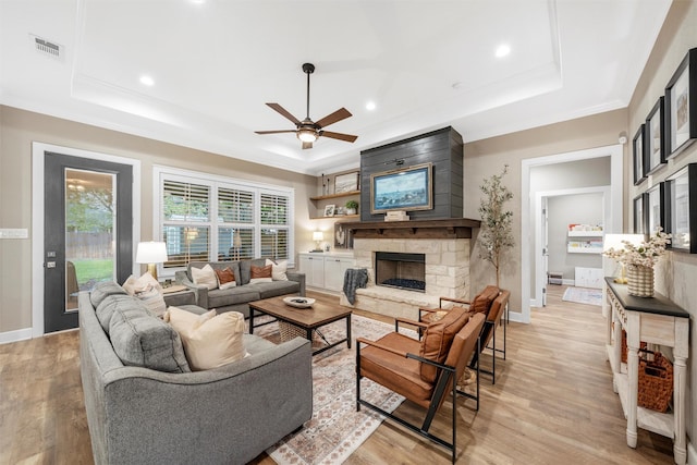 living room with a stone fireplace, light wood finished floors, visible vents, a ceiling fan, and a tray ceiling
