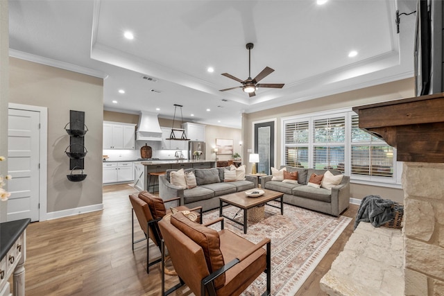 living area with a raised ceiling, crown molding, light wood-style flooring, and baseboards