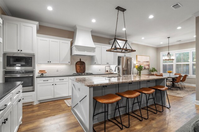kitchen featuring a kitchen island with sink, custom exhaust hood, appliances with stainless steel finishes, a sink, and visible vents