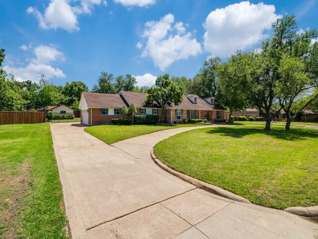 view of front facade featuring a front lawn, driveway, brick siding, and fence