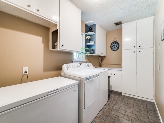 clothes washing area featuring a textured ceiling, stone finish flooring, visible vents, separate washer and dryer, and cabinet space
