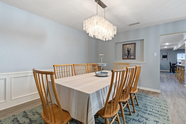 dining room featuring a notable chandelier, a wainscoted wall, visible vents, and wood finished floors